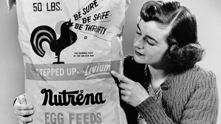 A woman holding a bag of Nutrena bag, providing nutrition for chickens.