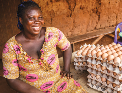 African woman sitting next to egg boxes and smiling at the camera