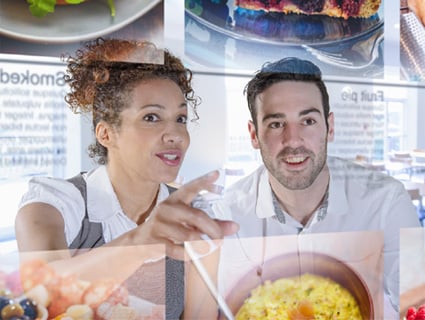 Woman smiling and pointing and man smiling, looking at food images