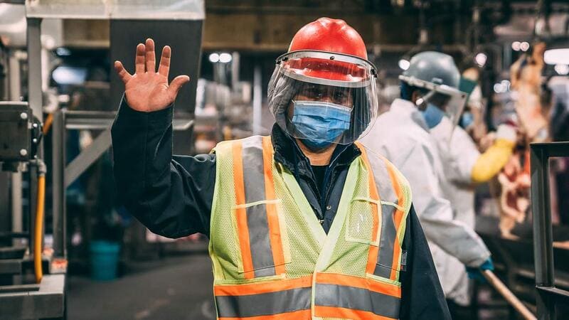 Plant worker in safety vest hard hat face shield and mask meat processing Protein CPS
