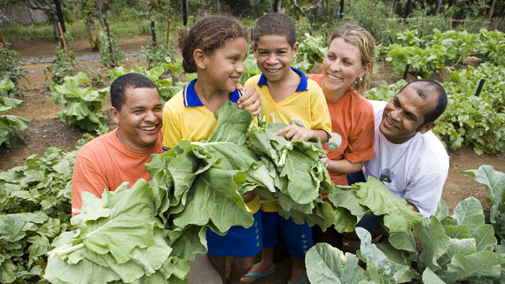 adults and kids in a vegetable garden holding salads image