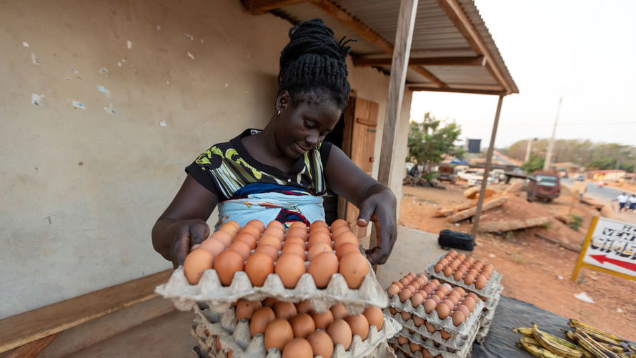 A woman in an agricultural community stacks containers of eggs on top of one another.