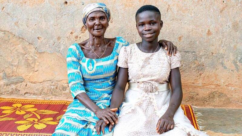 A woman embraces Anne (a young girl) and both smile at the camera