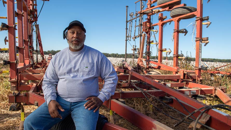 A Black farmer rests on farming machinery.