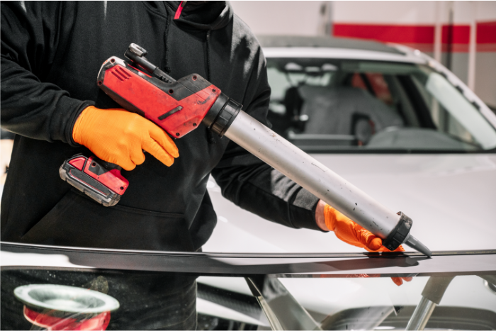 Glazier applies rubber sealant to car windshield in garage