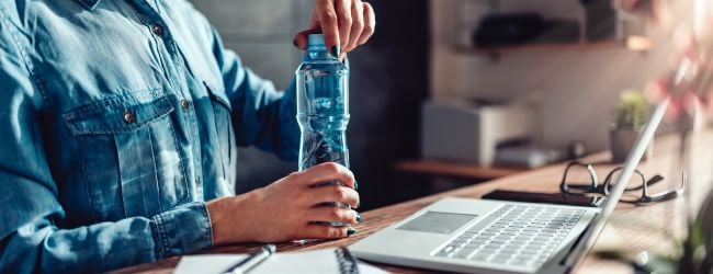 Person wearing a denim shirt opening a plastic water bottle