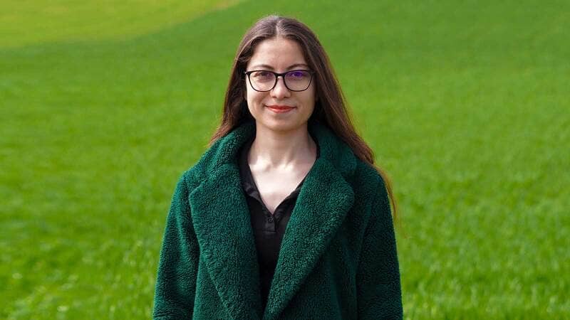 A young female farmer posing in front of a field.