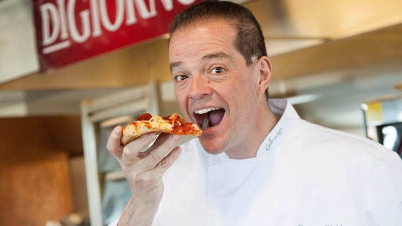 A male chef eats a piece of pizza.