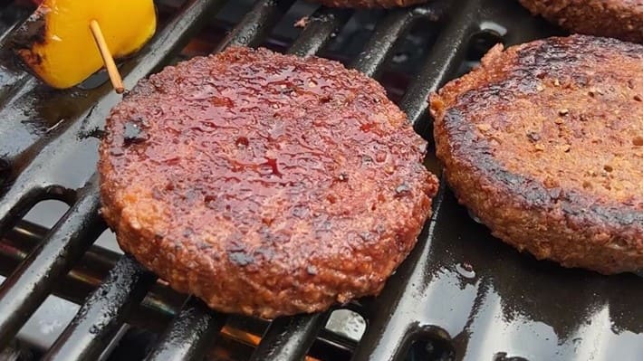 Plant-based burgers cooking on a grill.