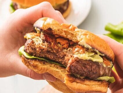 A person holding a plant-based burger that has a bite taken out of it. A person holding a plant-based burger that has a bite taken out of it.