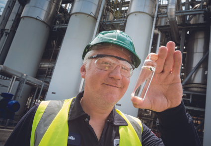 Employee holding small vial in front of manufacturing plant