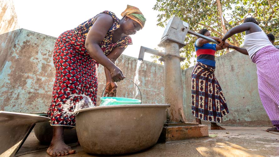 Women pump water at a well. Women pump water at a well.
