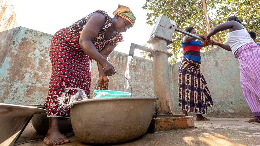 Women pump water at a well.