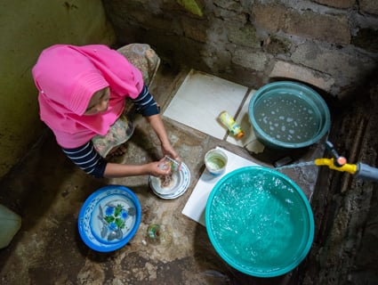 A young woman uses water to clean dishes.
