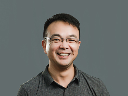 A man wearing glasses and a gray, collared shirt smiles. 