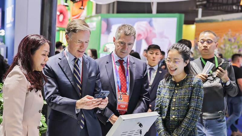 A group of CIIE visitors surround a digital screen and snap a photo on a mobile phone. 