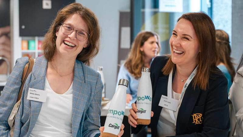 Two women laugh while holding water bottles commemorating the Empower event, organized by Cargill to celebrate women in trading. 