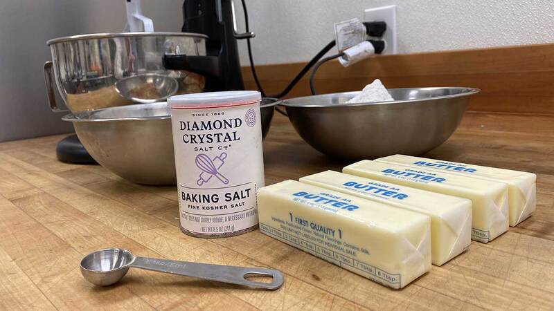 A container of Diamond Crystal Fine Kosher Baking Salt™ on a table next to butter and bowls.