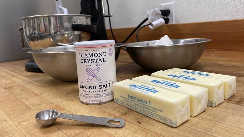 A container of Diamond Crystal Fine Kosher Baking Salt™ on a table next to butter and bowls. A container of Diamond Crystal Fine Kosher Baking Salt™ on a table next to butter and bowls.