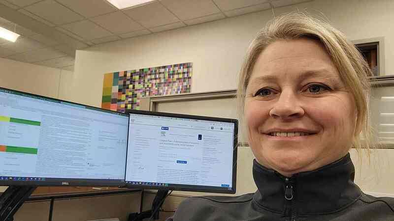 A woman smiles while sitting in front of a computer screen with a food science article on it. A woman smiles while sitting in front of a computer screen with a food science article on it.