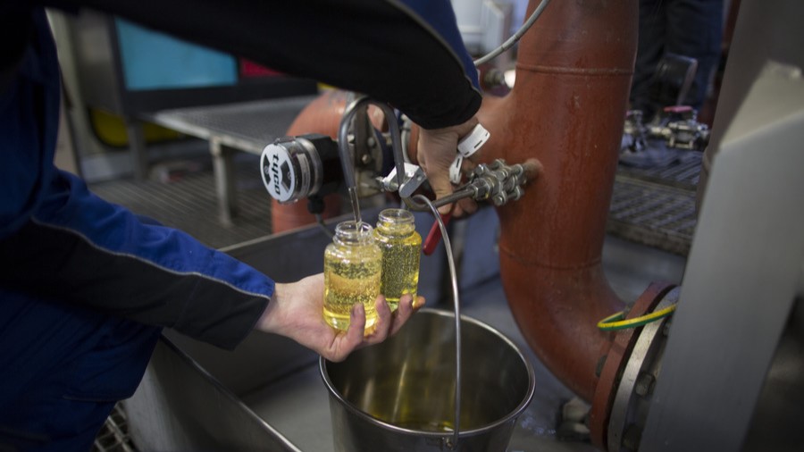 A Cargill employee pours oil into a clear glass container. A Cargill employee pours oil into a clear glass container.