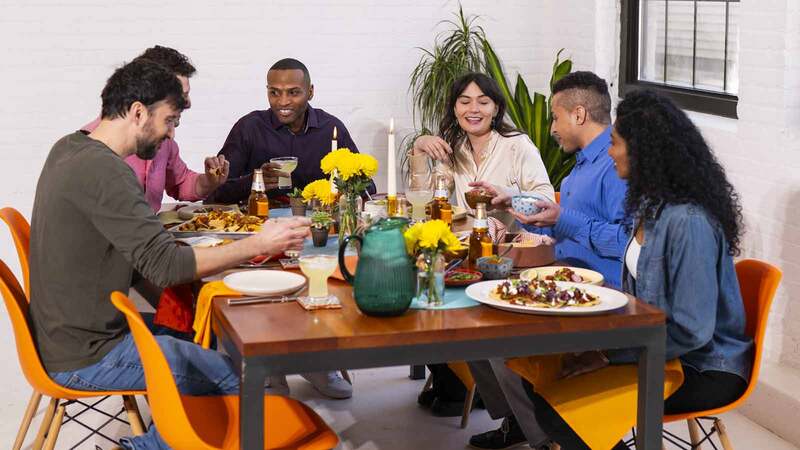 A group of young people sitting around a table eating A group of young people sitting around a table eating