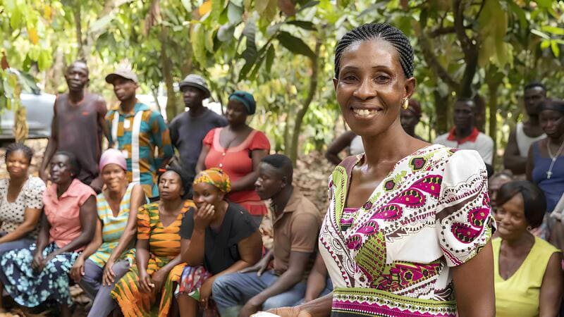 A female cocoa farmer standing with a group of women smiling. A female cocoa farmer standing with a group of women smiling.