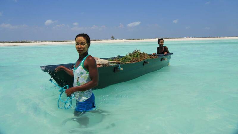 two women seaweed farmers with a boat in the water.