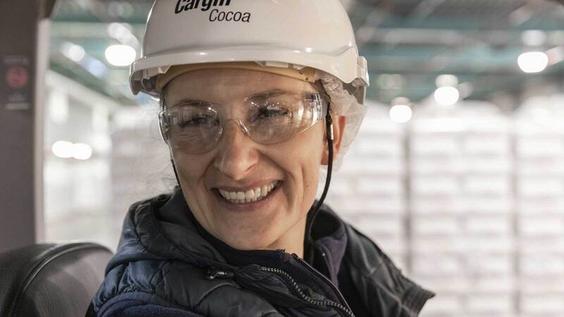 A woman in a hard hat and safety glasses smiles.