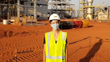 A woman in a hard hat and safety glasses smiles.