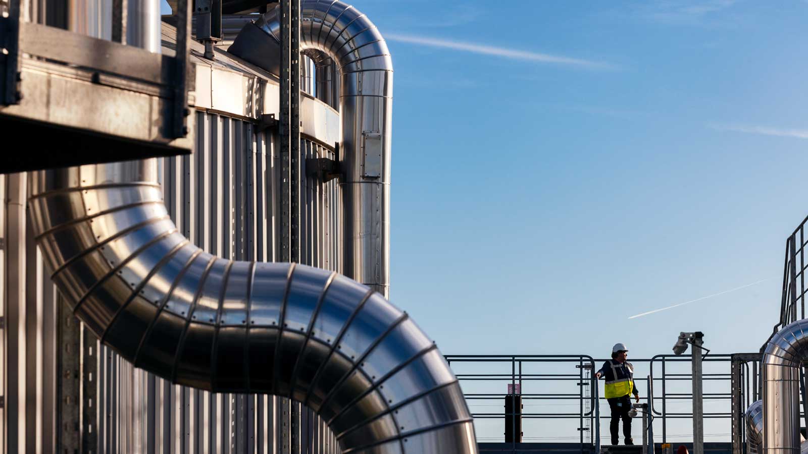 A worker wearing a hard hat and glasses looks out over a plant that makes bioenergy and biofuel. A worker wearing a hard hat and glasses looks out over a plant that makes bioenergy and biofuel.