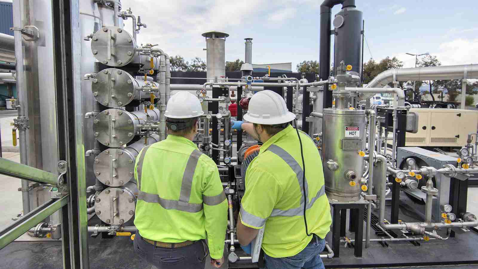 Two men point to a machine producing biogas. 