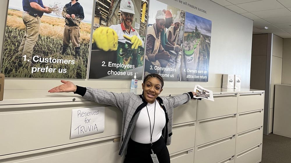 A woman poses next to a wall of posters at a corporate office. A woman poses next to a wall of posters at a corporate office.