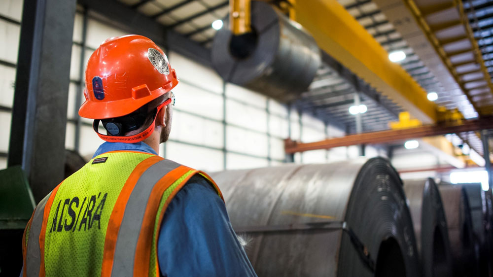 A Cargill employee watches as a roll of metal is moved by a crane. A Cargill employee watches as a roll of metal is moved by a crane.