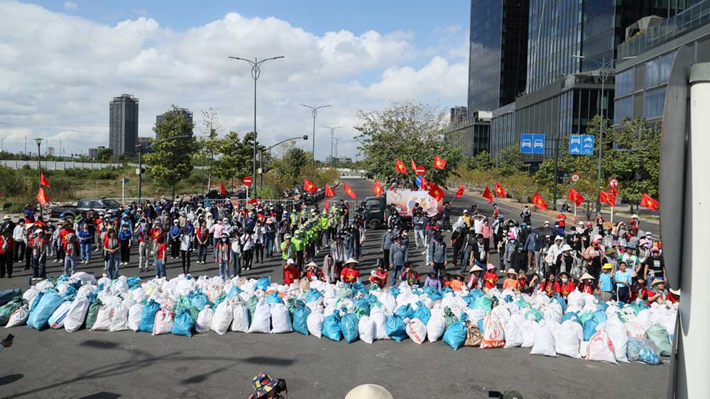 A large group of people with Vietnam flags pose next to hundreds of trash bags. A large group of people with Vietnam flags pose next to hundreds of trash bags.