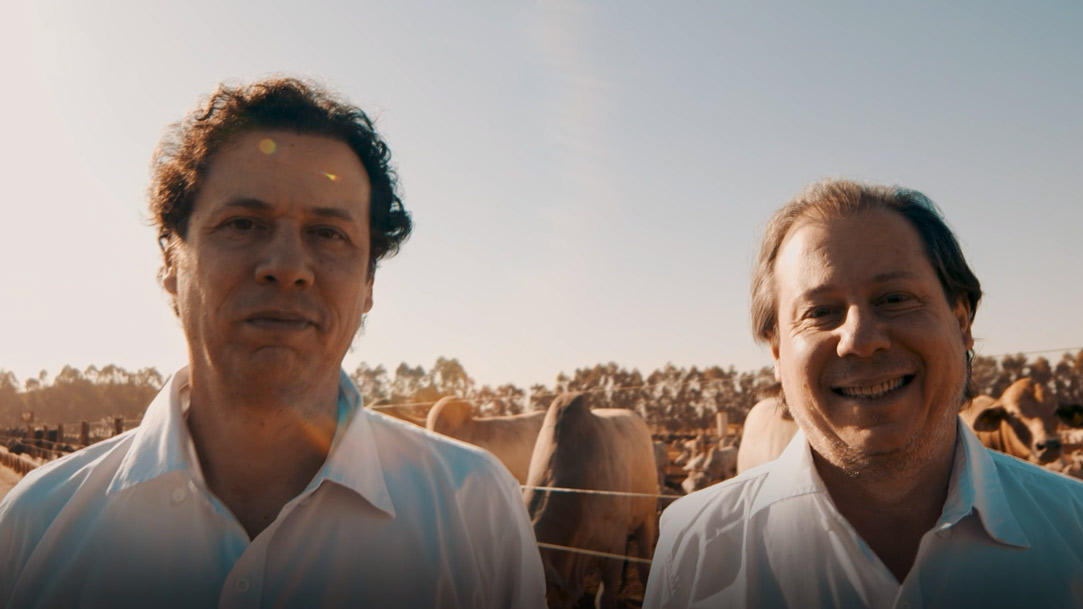 Dois homens sorrindo em um escritório, rodeados de livros. 