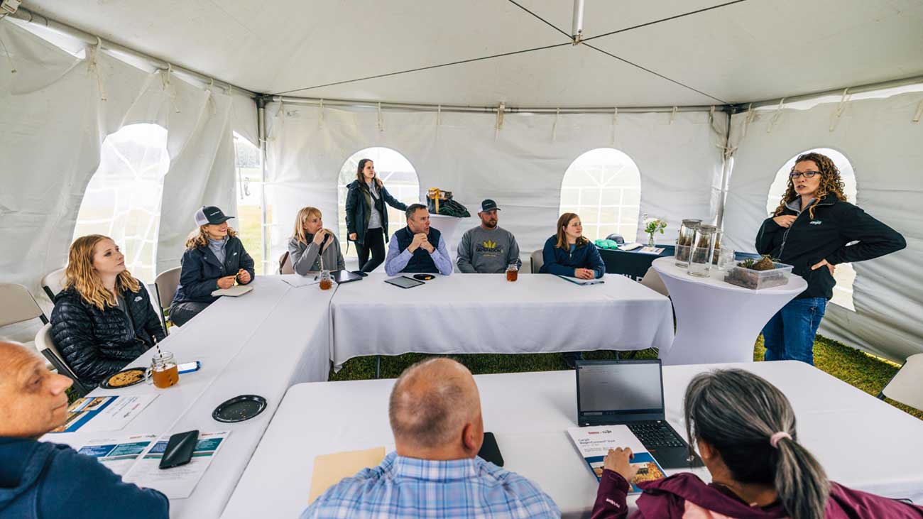 A woman gives a presentation in a white tent set up in farm field. A woman gives a presentation in a white tent set up in farm field.