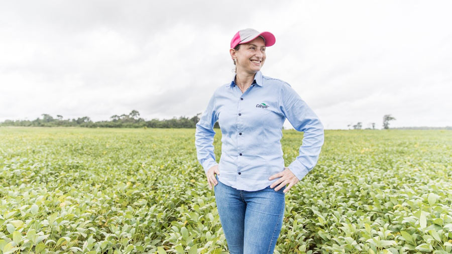 A smiling woman stands in a field of crops. 
