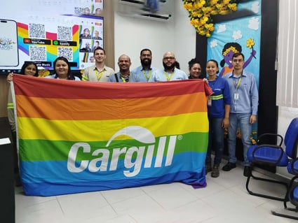 A group of cargill employees posing with a large pride flag inside an office A group of cargill employees posing with a large pride flag inside an office