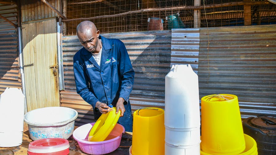 A poultry farmer in blue coverall disinfects his bird feeders and drinkers. A poultry farmer in blue coverall disinfects his bird feeders and drinkers.