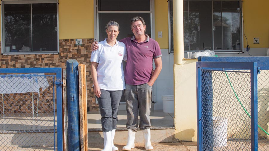 A female and male farmer stand together in front of their home. A female and male farmer stand together in front of their home.