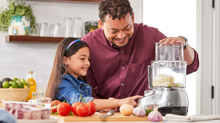 : Father and daughter using a food processor while preparing a meal.