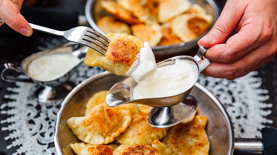 A person with pierogi on a fork dips it into a white sauce in a small pitcher. 