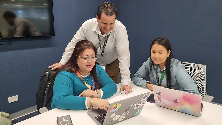A group of three people meet in a conference room and look at a computer screen