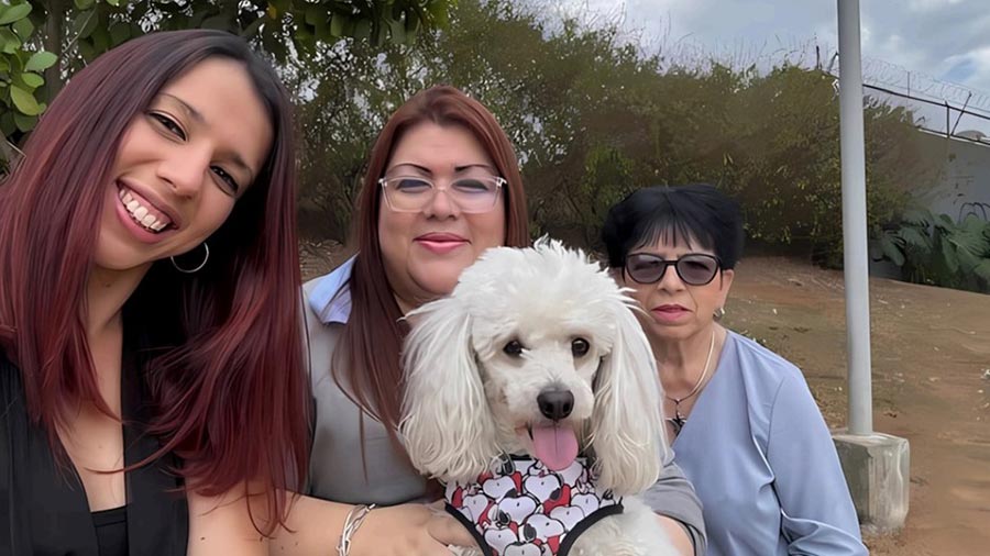 A group of three women and a dog sit for a photo. A group of three women and a dog sit for a photo.