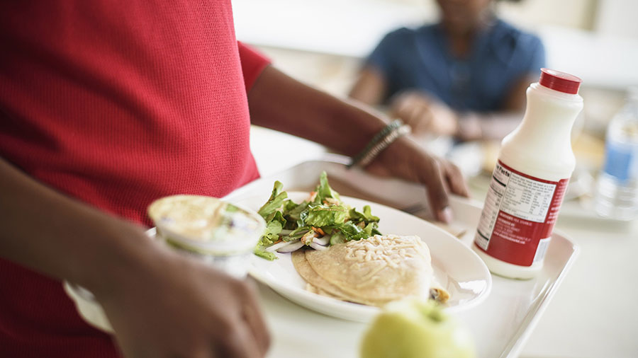 A child holds a tray with salad, tortillas and a bottle of milk. A child holds a tray with salad, tortillas and a bottle of milk.
