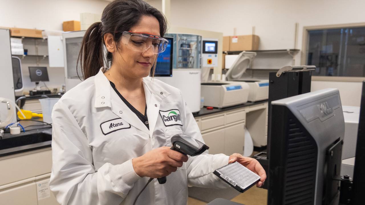 A Cargill crop innovation scientist scans a small tray of plant simples while standing in front of a computer. A Cargill crop innovation scientist scans a small tray of plant simples while standing in front of a computer.