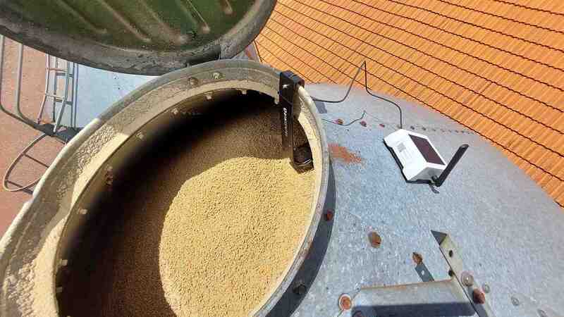  A white BinSentry sensor is plugged into the top of a large grain bin.  