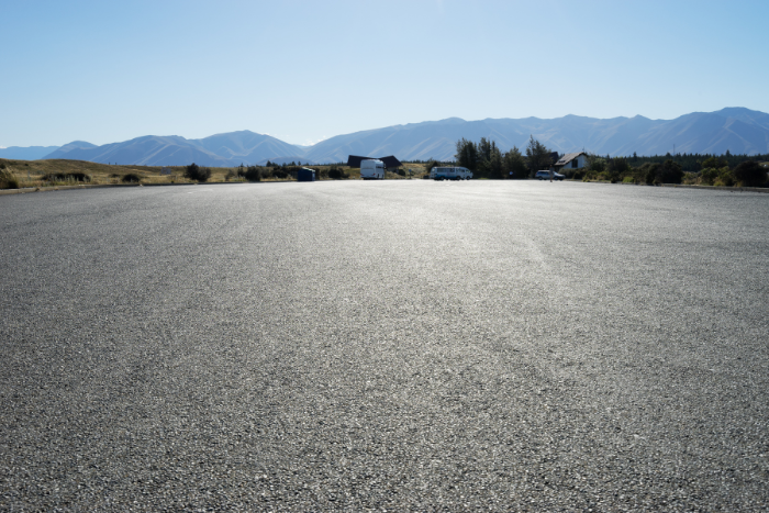 Freshly paved asphalt surface with mountains and trees in the background under clear blue sky