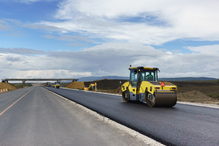 Yellow road roller compacting fresh asphalt on a highway construction site under cloudy sky
